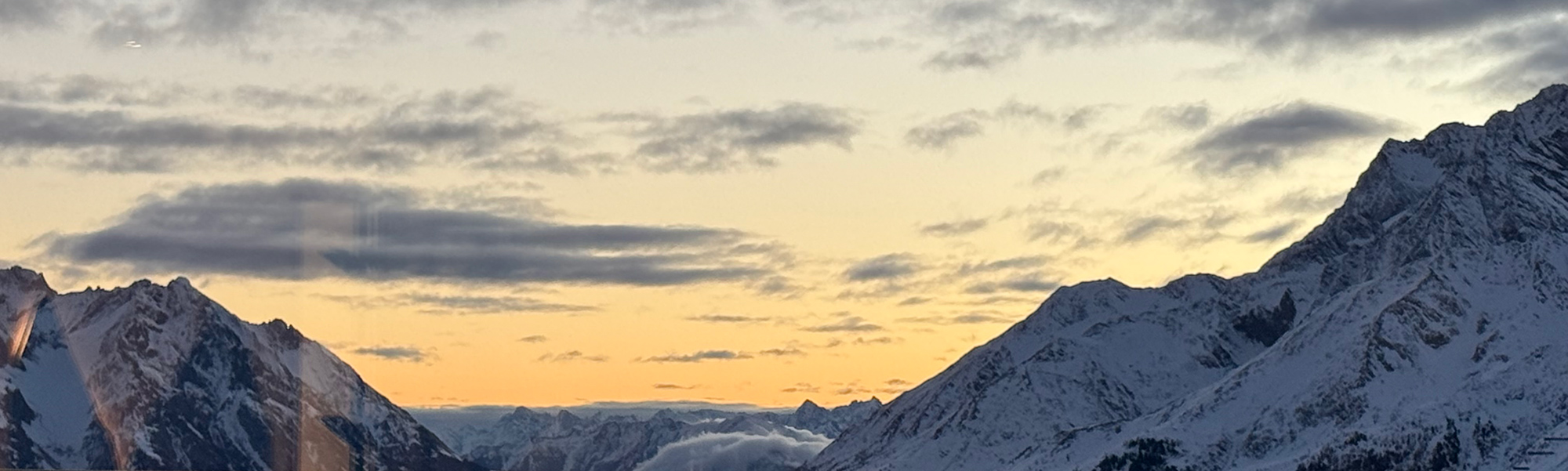 Winterpanorama in St. Anton am Arlberg mit verschneiten Bergen im Sonnenuntergang und goldenem Himmel.