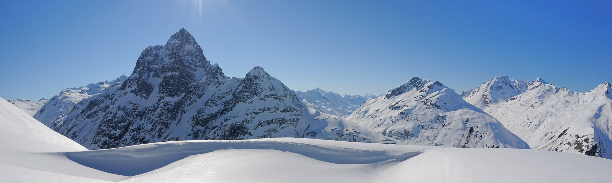Schneebedeckte Berggipfel unter strahlend blauem Himmel, markanter Felsgipfel.